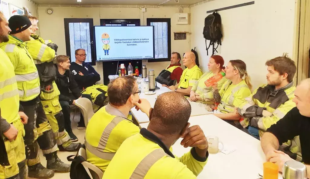 Workers sitting at a table in a construction site break room watching at a digital signage display